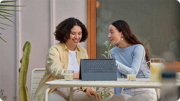 Two people outside sitting at a table, smiling, and looking at a tablet.