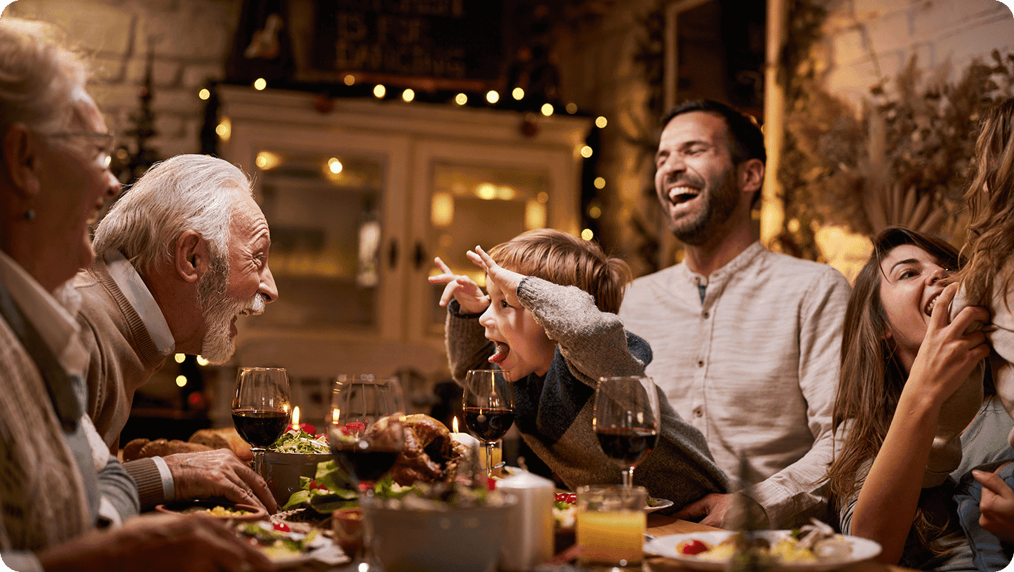 Multi-generational holiday gathering around a dining table with festive food, candles and seasonal décor.