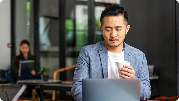 One person in the front using a laptop. Another person in the background passing by. 