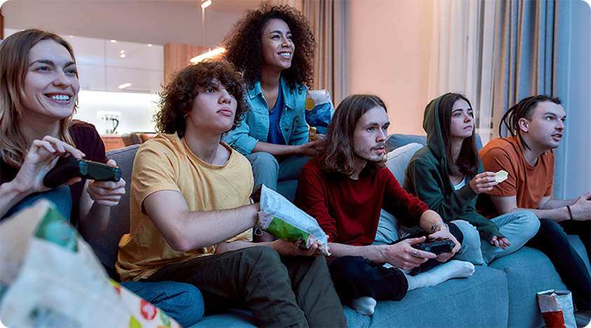 Group of people sitting on a couch, smiling and focused while playing a console game together with controllers.