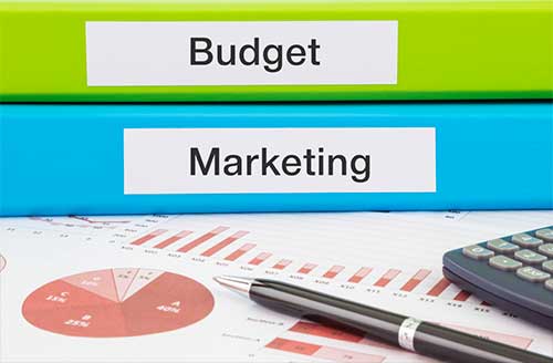 Close up of a desk with a pen, a calculator, and two folders labeled Budget and Marketing.