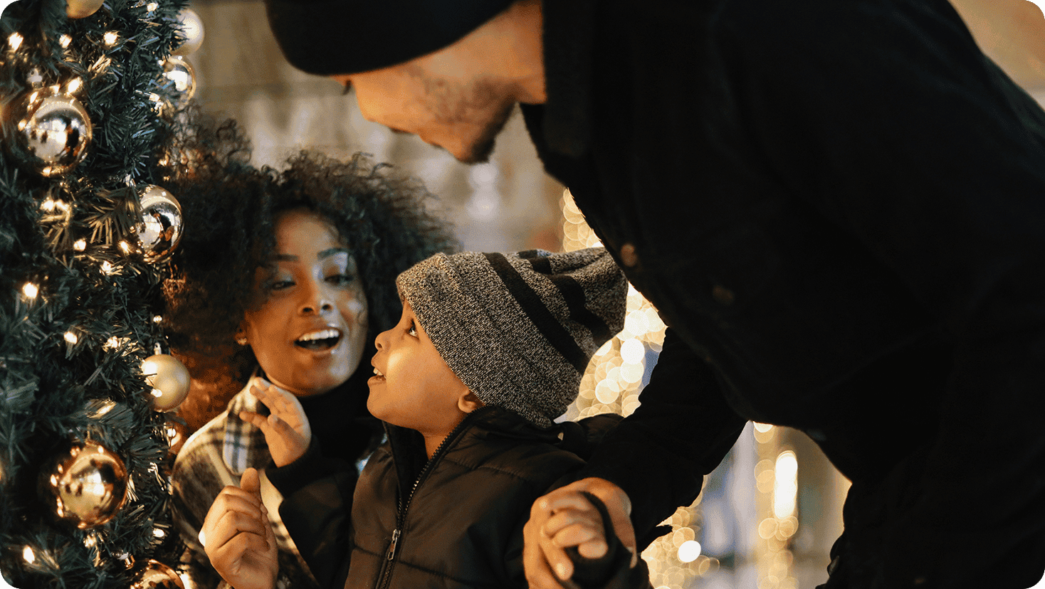 People gathered beside a decorated holiday tree, looking at ornaments and festive lights.