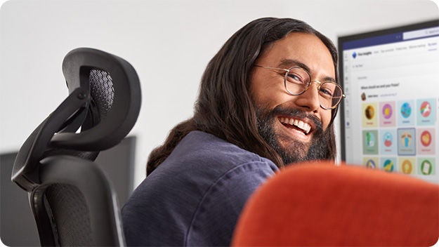 A person sitting at a desktop computer looking at the camera and smiling.