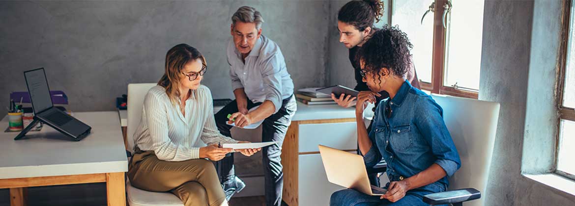 A woman holds a piece of paper while other people around her look and point at it and discuss.