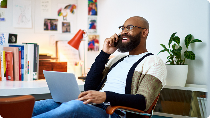 A smiling man talking on the phone while working on his computer.