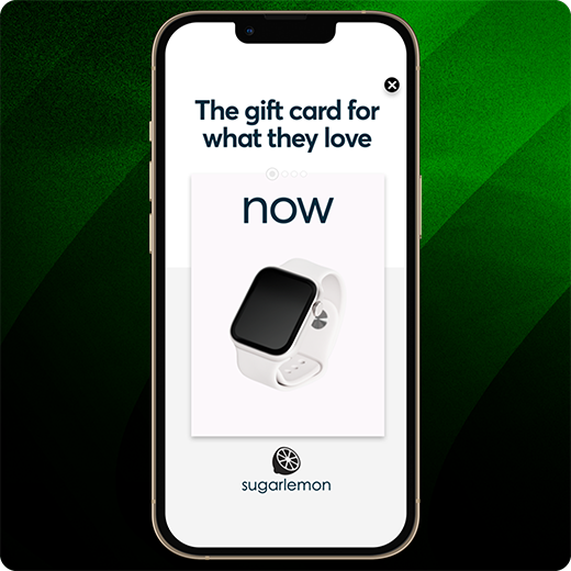 Smartphone displaying a Sugarlemon ad with the headline “The gift card for what they love,” featuring an image of a white smartwatch and the word “now” in bold text, set against a green striped background.