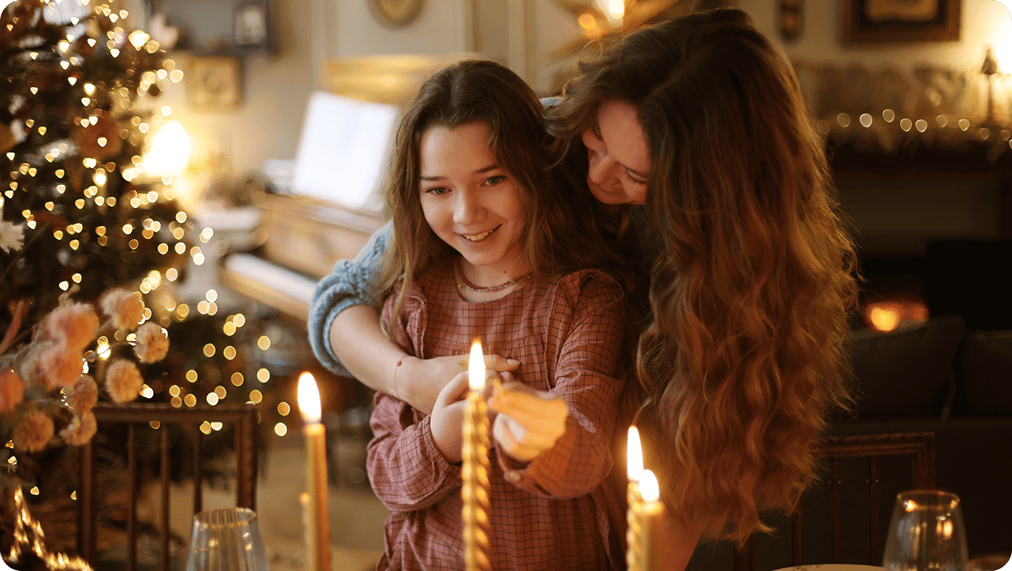 Child and adult gathered around a table with candles and seasonal decorations in a festively decorated home.