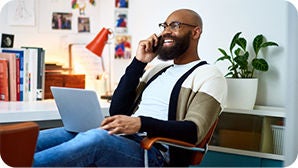 A smiling man talking on the phone while working on his computer.