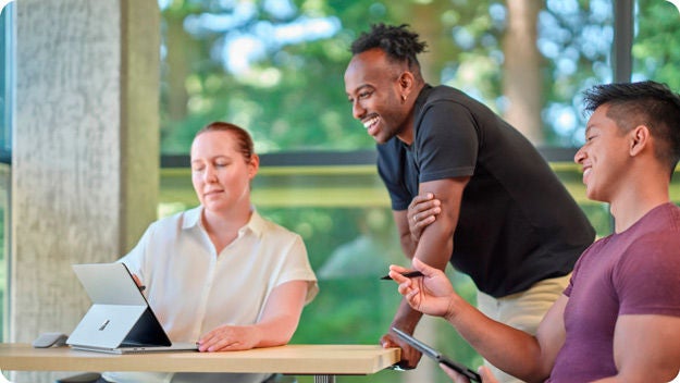 Three people collaborating over a tablet. One person is standing the other two are seated.