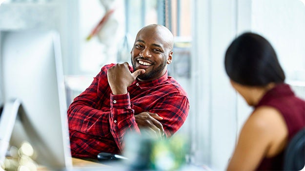 Two people sitting at a desk, one person in smiling at the other.