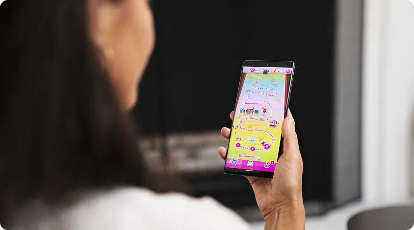 Person holding a smartphone and viewing a colorful map screen in Candy Crush Saga.