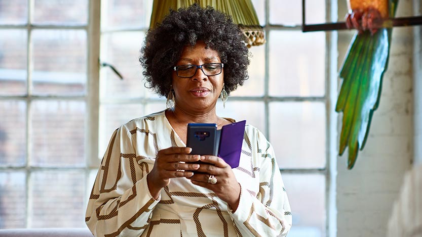 A person works on their phone in their living room with a colorful parrot statue in the background.