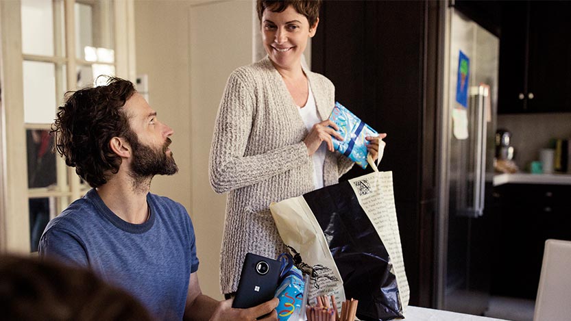 A man and a woman hold gifts in their hands and the man looks at the woman while she smiles.