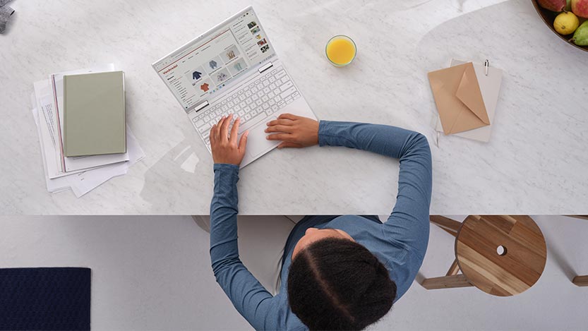 A woman seen from above works on a laptop computer while sitting at a table.