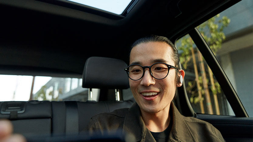 A man inside a car smiles while looking at his phone.