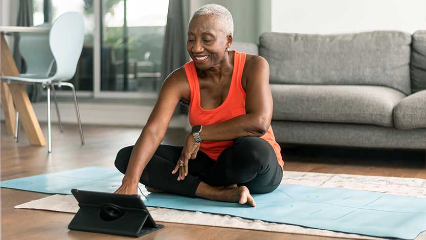 Woman sitting on a yoga mat interacting with a tablet.