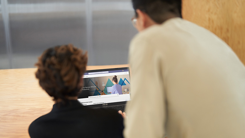 A man and woman seen from behind work on the same laptop.