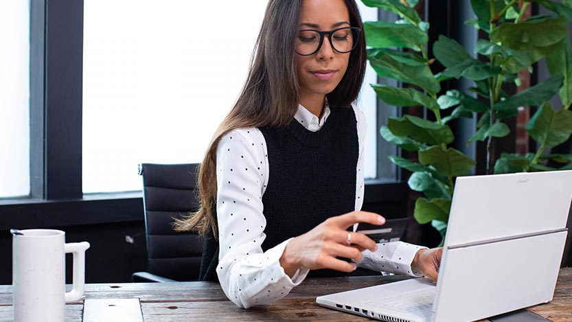 A woman in an office makes an online purchase while holding her card.