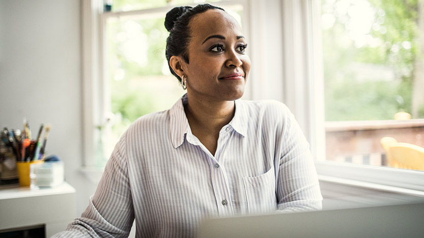 A woman sitting near a window smiles while looking away from the camera.