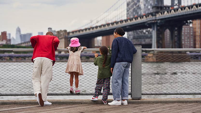 A group of people standing by the water looking at a bridge.