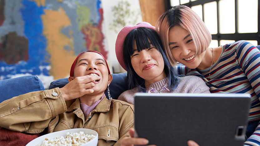 Three people smile while interacting with a tablet.