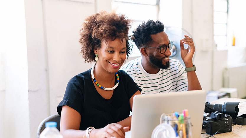 Two smiling people using a laptop.