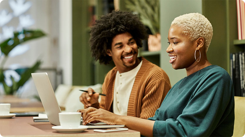 Two people smiling while working on a laptop at work