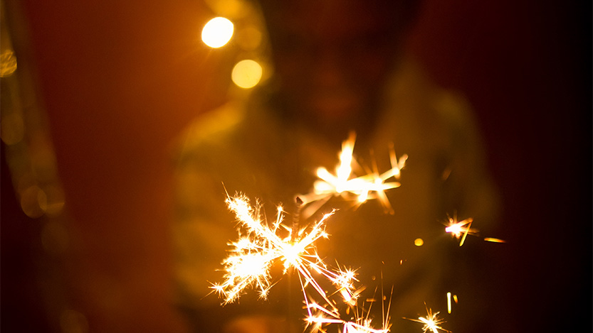 Person smiling while holding a festive sparkler