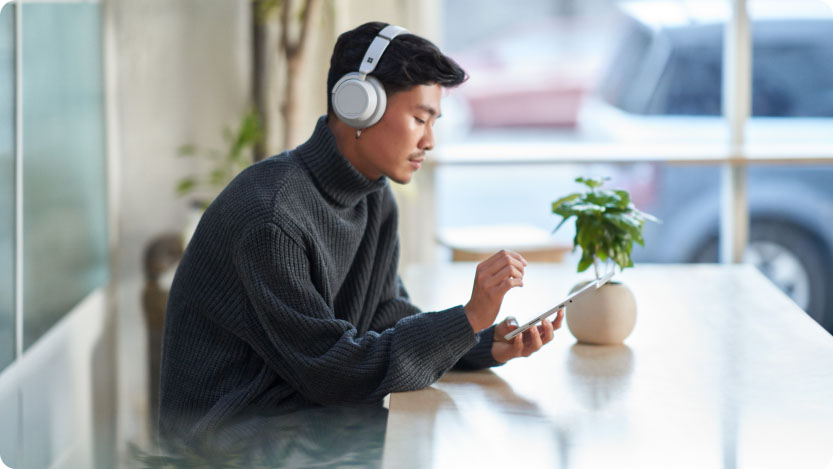 Person with headphones using a tablet while sitting near a window at home.