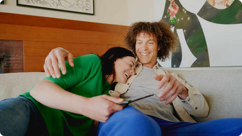 A couple smiles while hugging each other on a couch.