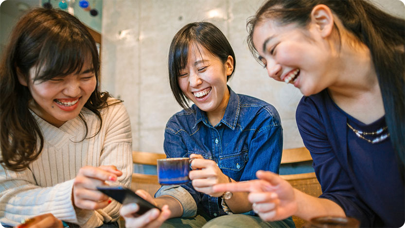 Drei lachende Kolleginnen schauen auf ein Smartphone.