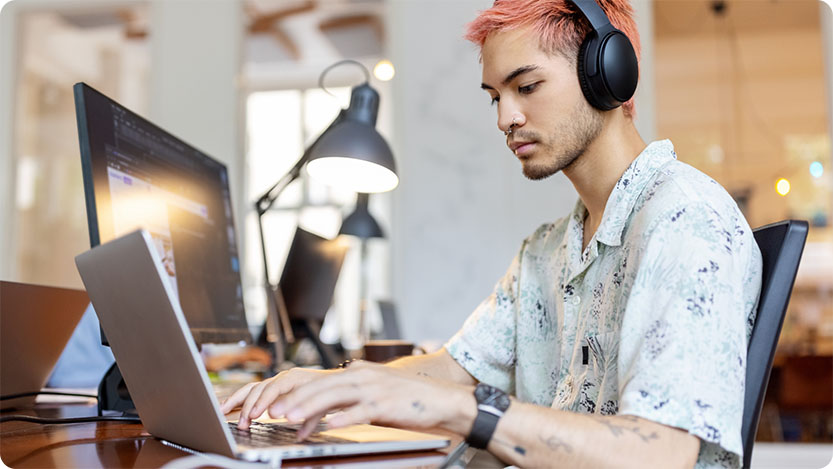 Personne avec des écouteurs, assise à un bureau, travaillant sur un ordinateur portable.