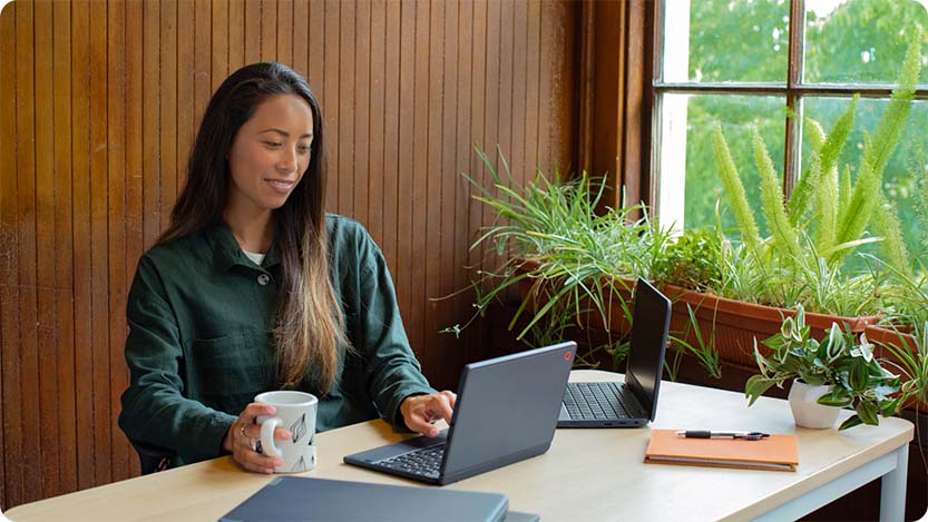 Person sitting at a table with a cup and two laptops.