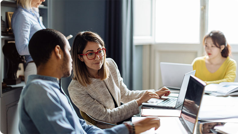 Four people in a room, two in the background and two upfront using laptops.