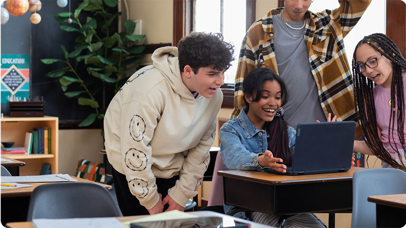 Four people in a classroom looking surprised at a laptop.