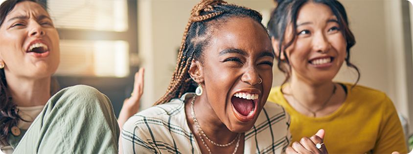 Three people sitting together, laughing and cheering while playing a video game with controllers.