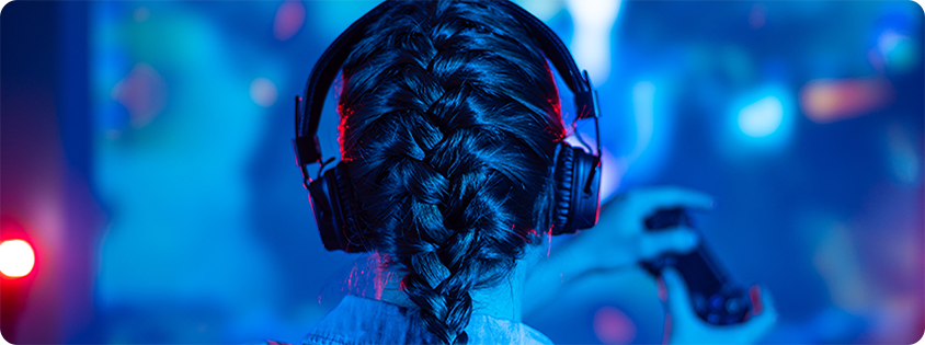 Person seen from behind wearing a headset and holding a controller while playing a game in a neon-lit room.