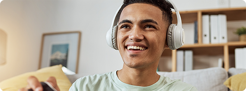 Young person smiling while wearing headphones and playing a video game with a controller 