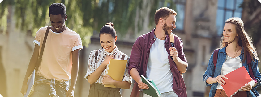 Group of college-age friends walking outdoors on campus, smiling and carrying notebooks and backpacks. 