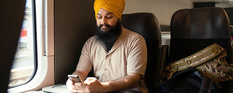 A man sits on a train and uses his cellphone. His bags are next to him on an empty seat.