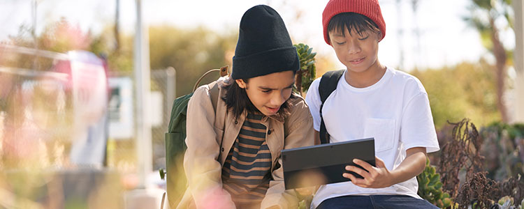 Zwei Kinder sitzen im Freien und schauen auf ein Tablet.