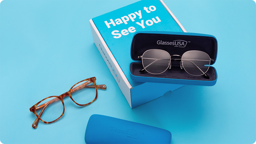 Eyeglasses in blue cases with branded packaging from GlassesUSA.com, featuring the slogan 'Happy to See You'.