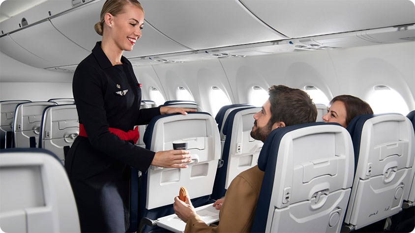 Two passengers sitting on a plane and a flight attendant serving a drink.