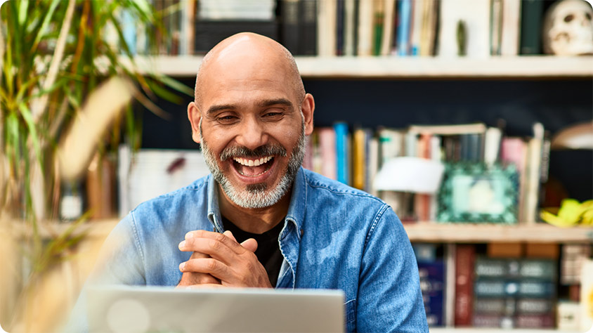 Close up picture of a person indoors smiling while using a laptop.