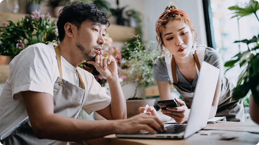 Two people indoors looking at a laptop on a desk.