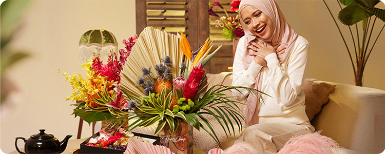 Une personne assise devant un grand bouquet de fleurs, souriante.
